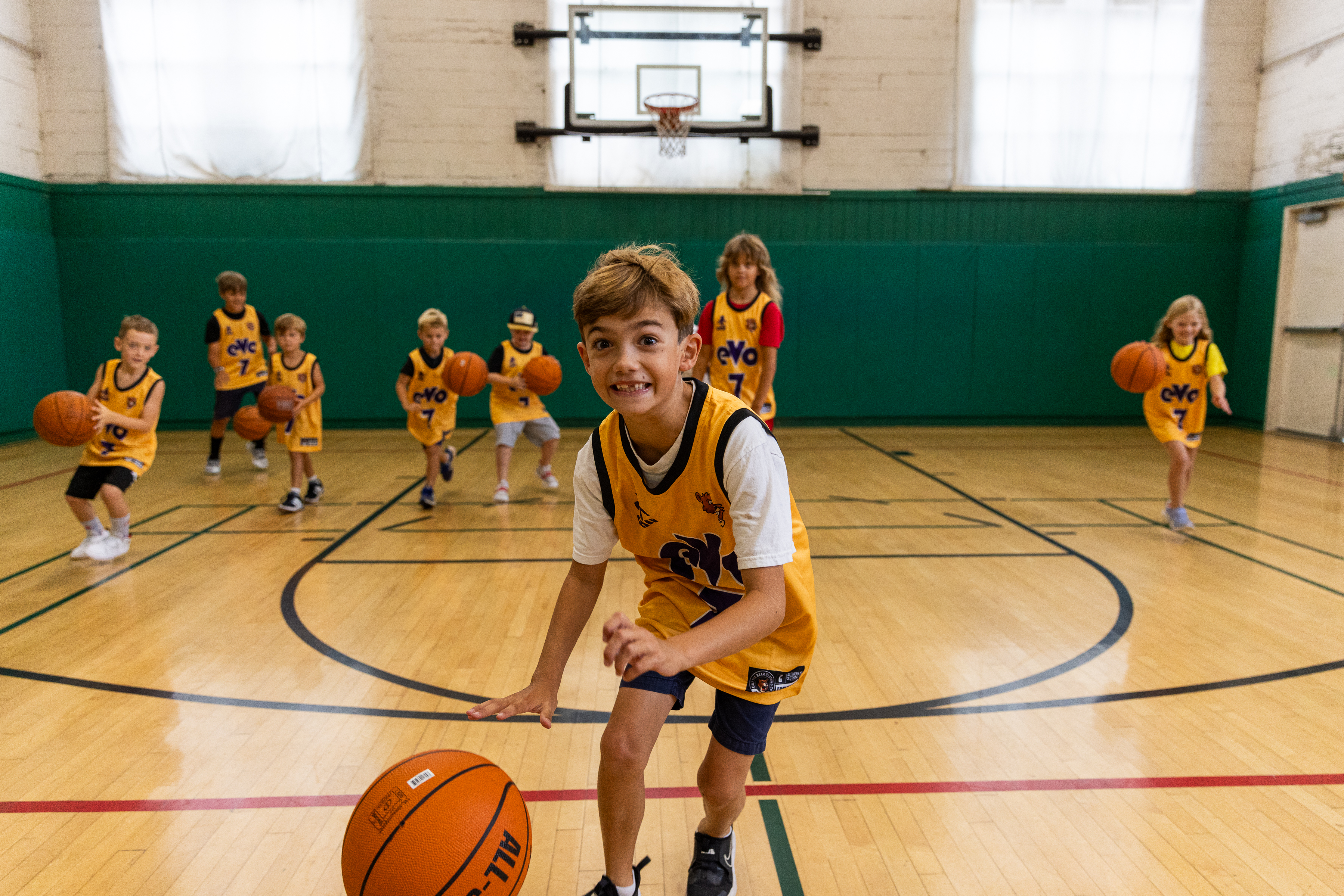 Camper dribbles a basketball toward the camera with a large group in the background dribbling as well.