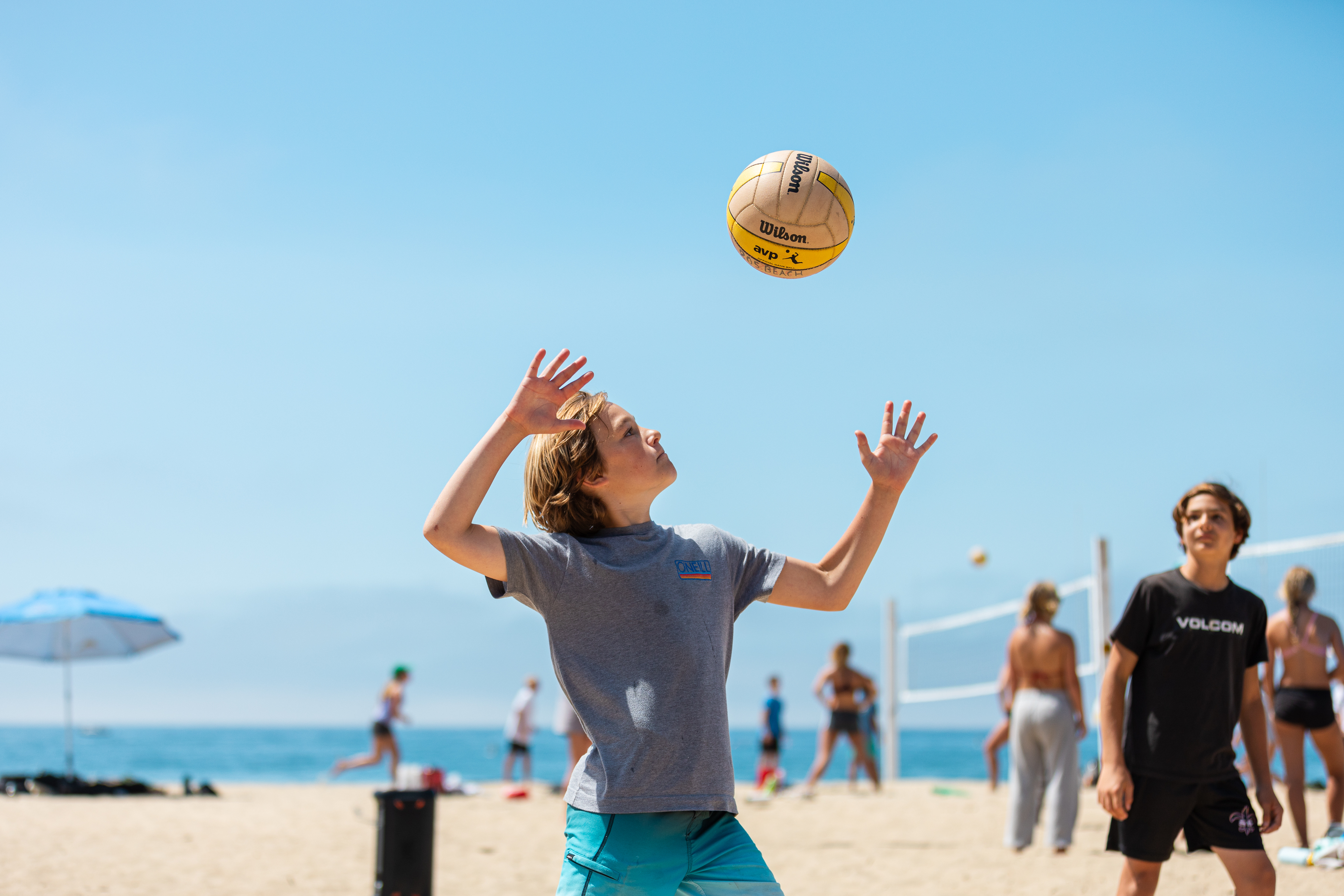 Camper serves a beach volleyball at East Beach