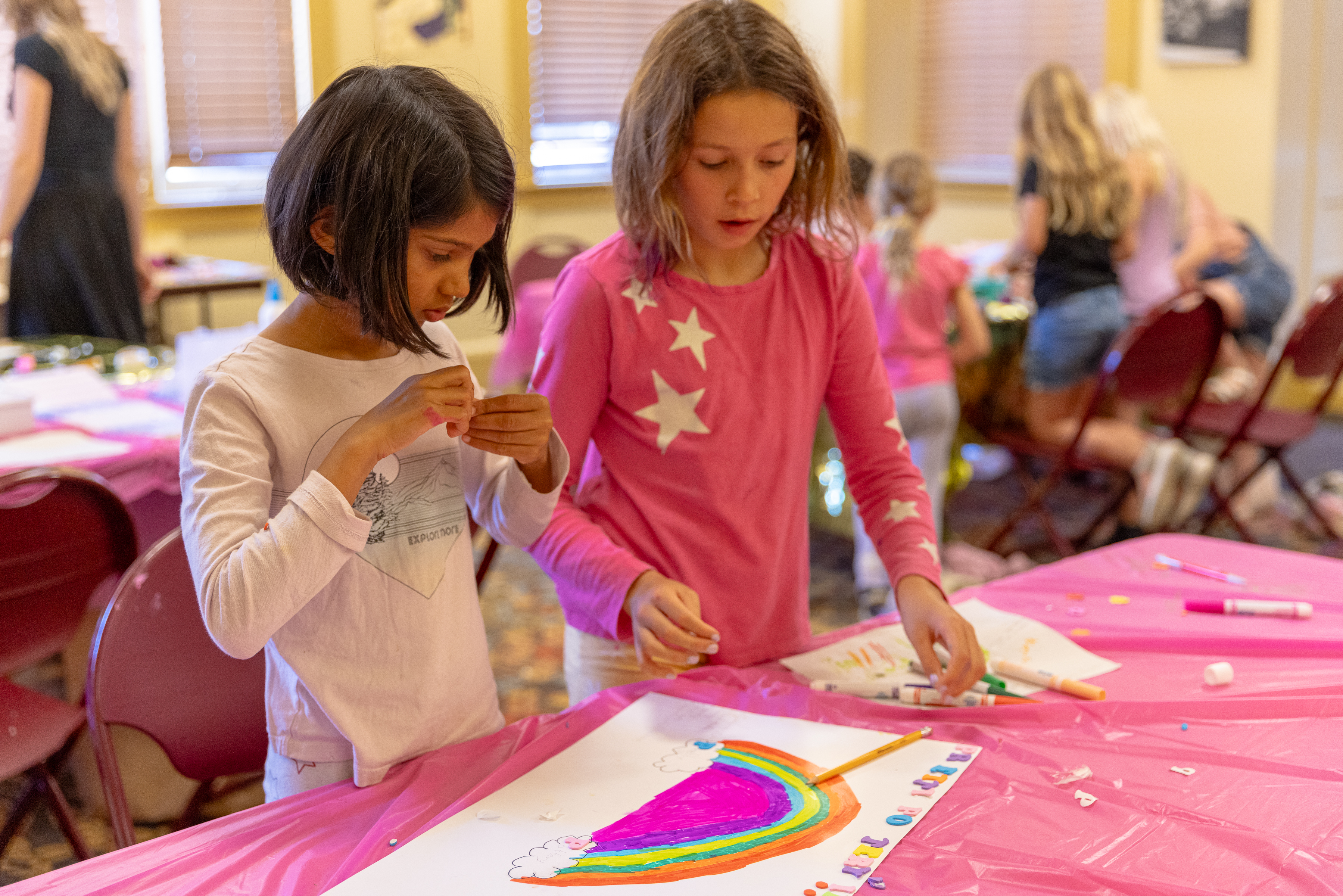 Two campers smile as they work on their rainbow artwork
