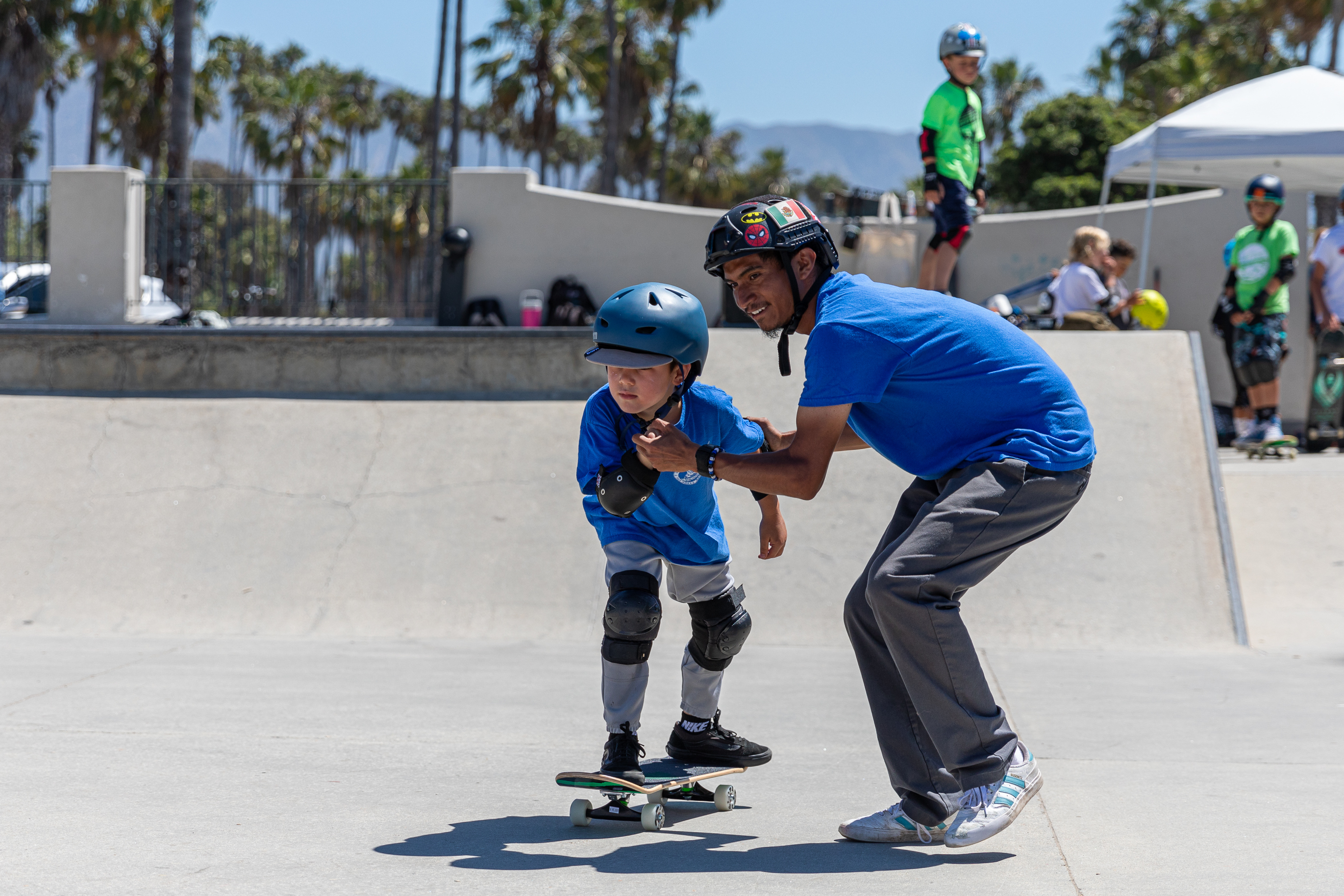 Camper riding a skateboard is helped by a counselor holding their hands