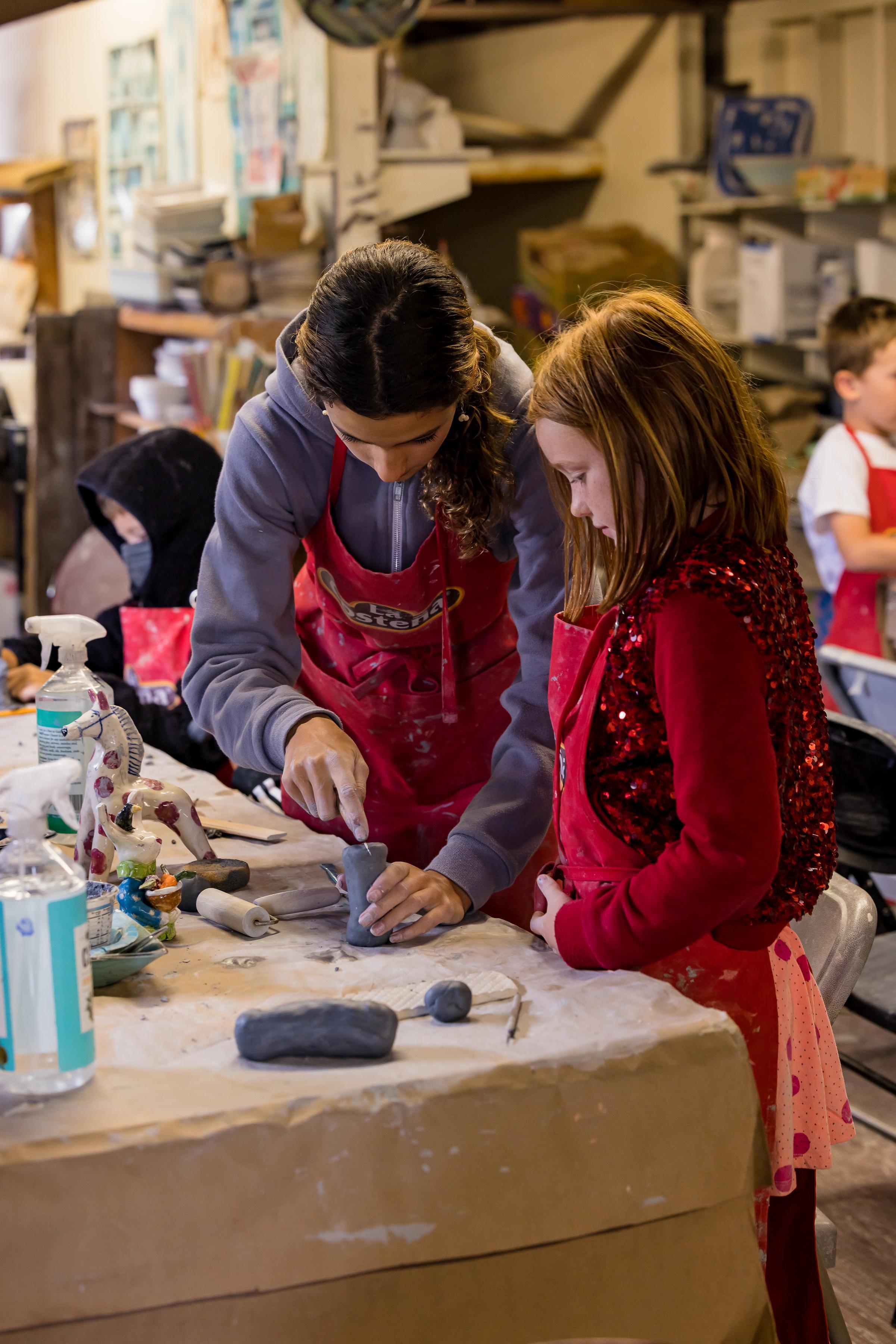 Ceramics camp counselor teaches a young camper 