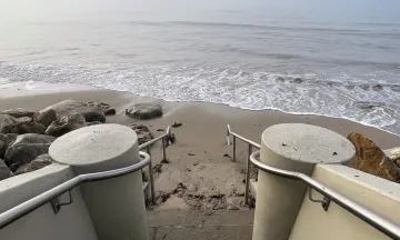 Photo shows the bottom of the Thousand Steps beach on the Mesa. Image depicts the new handrail and steps with the sand and ocean in view. 
