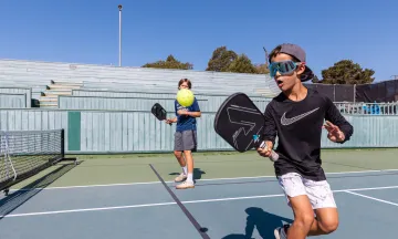 Camper backhands the ball over the net in pickleball camp 