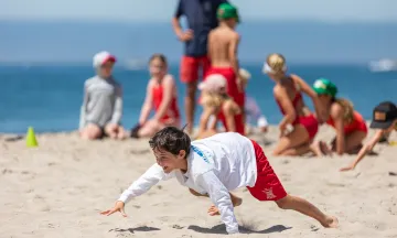 Junior Lifeguard bear crawls across the sand in a relay competition