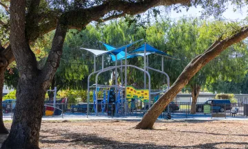 A tall colorful playground behind a grove of oak trees in Eastside Neighborhood Park