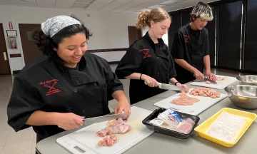 Participants of the Chef Apprentice Program practice their knife skills as they dice chicken