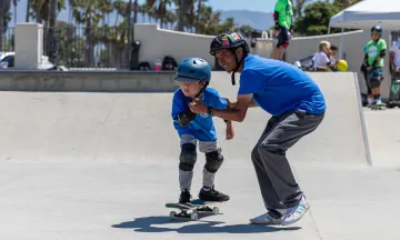 Camper riding a skateboard is helped by a counselor holding their hands
