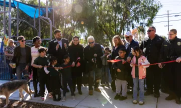 Community leaders and members cut a ribbon in front of a new playground at Eastside Park