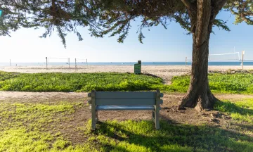 East Beach Park bench with ocean view and volleyball courts in background