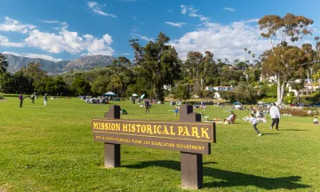 Mission Historical Park sign with people enjoying the grassy area in the background