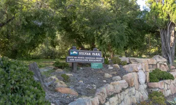 Sylvan Park sign surrounded by green foliage and a stone wall below
