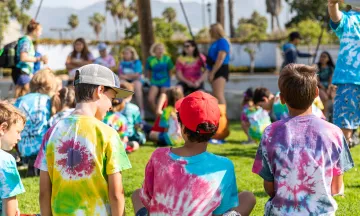 Campers in tie-dye shirts sit and focus on the camp counselors