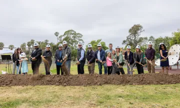 Groundbreaking guests wearing hard hats and holding gold shovels 