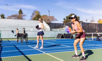 Two adult pickleball players smile as they await a serve