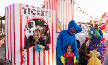 Trunk or Treat - Parks and Recreation Staff posing in a circus ticket booth and a creepy blue costume figure taking a photo with a little kid in a spiderman costume