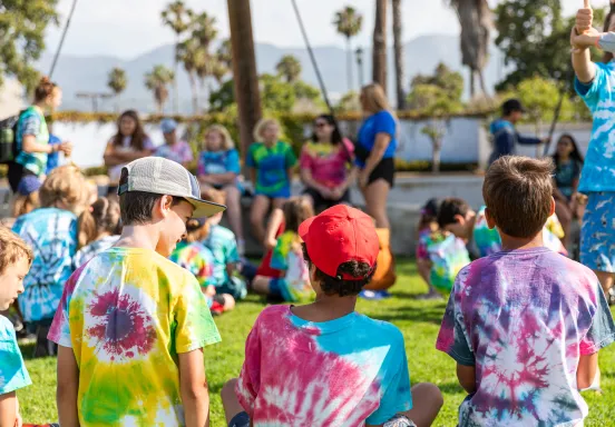 Campers in tie-dye shirts sit and focus on the camp counselors
