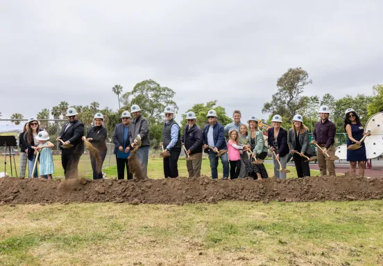 Groundbreaking guests wearing hard hats and holding gold shovels 