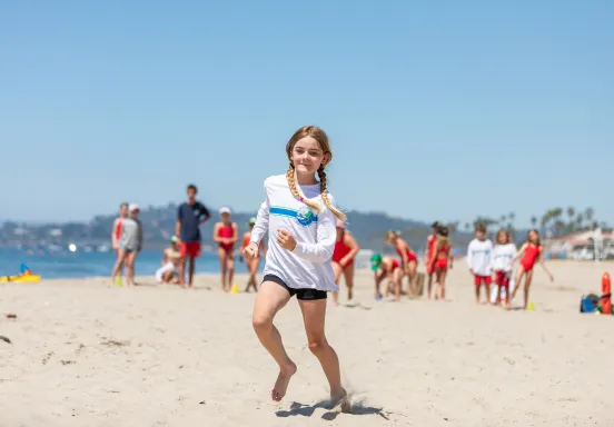 girl in white tshirt and black shorts running in the sand on the beach