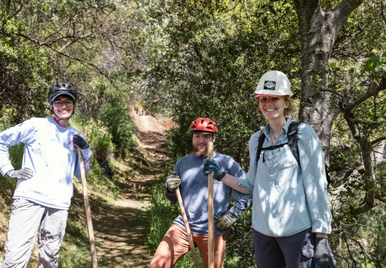 Volunteers on a trail smile while holding tools