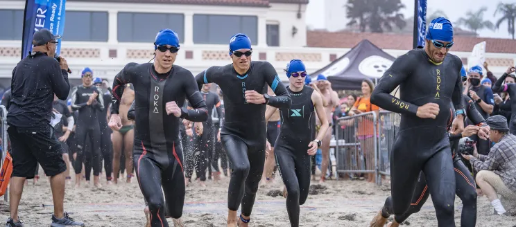 Triathletes in wetsuits running on sand