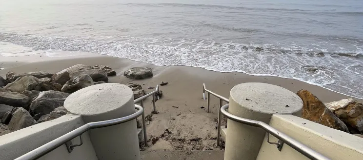 Photo shows the bottom of the Thousand Steps beach on the Mesa. Image depicts the new handrail and steps with the sand and ocean in view. 