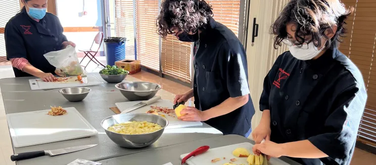 Three participants of the Chef Apprentice Program prep ingredients