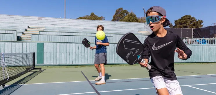 Camper backhands the ball over the net in pickleball camp 