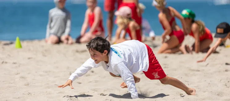 Junior Lifeguard bear crawls across the sand in a relay competition