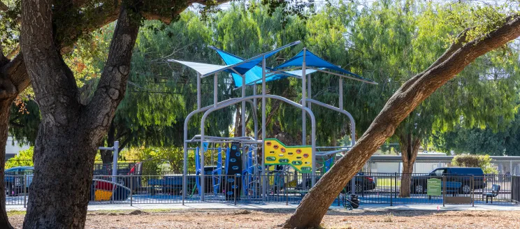 A tall colorful playground behind a grove of oak trees in Eastside Neighborhood Park