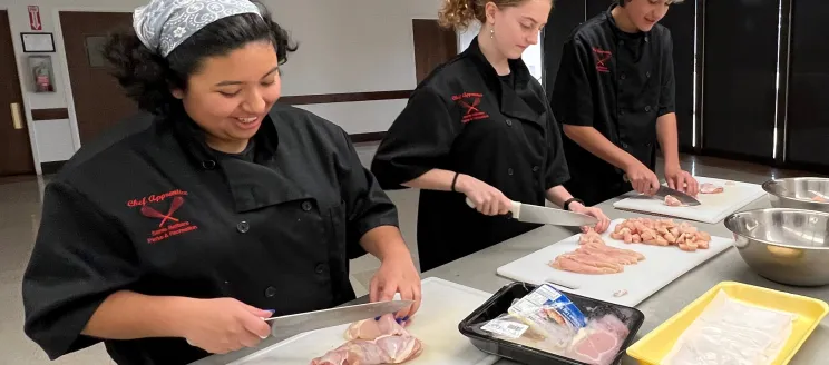 Participants of the Chef Apprentice Program practice their knife skills as they dice chicken