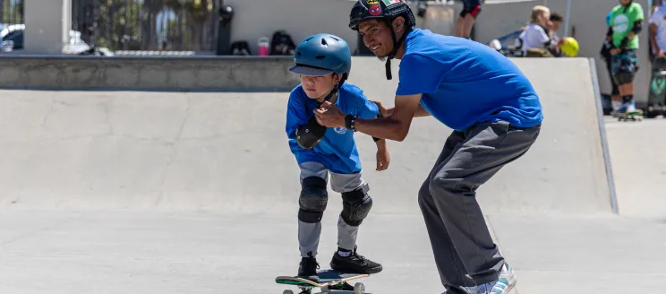 Camper riding a skateboard is helped by a counselor holding their hands