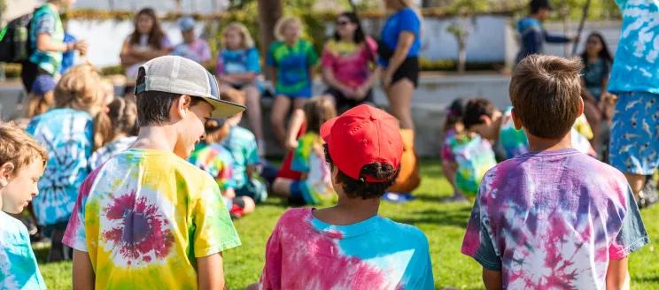 Campers in tie-dye shirts sit and focus on the camp counselors