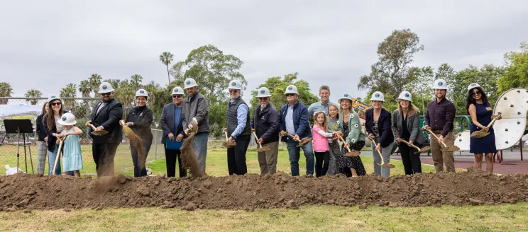 Groundbreaking guests wearing hard hats and holding gold shovels 