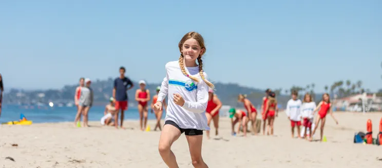 girl in white tshirt and black shorts running in the sand on the beach