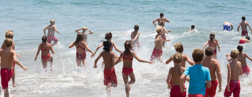 Participants in Junior Lifeguards run into the ocean