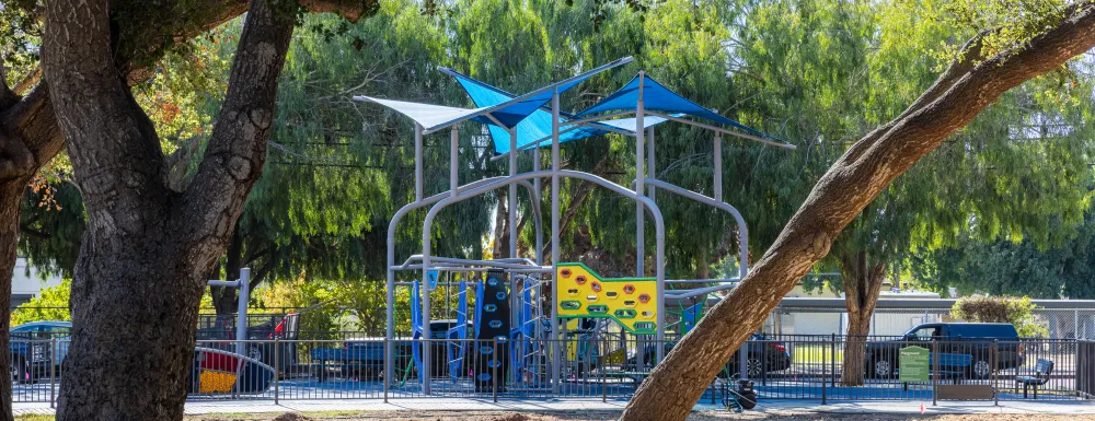 A tall colorful playground behind a grove of oak trees in Eastside Neighborhood Park