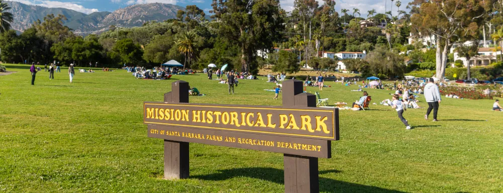 Mission Historical Park sign with people enjoying the grassy area in the background