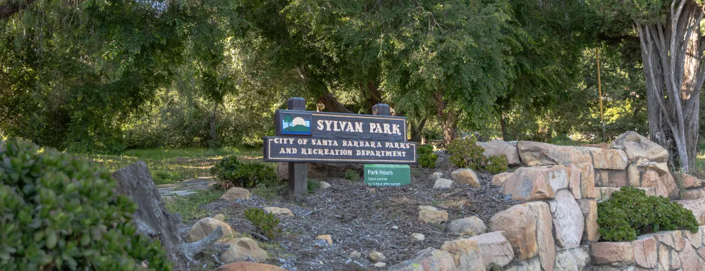 Sylvan Park sign surrounded by green foliage and a stone wall below