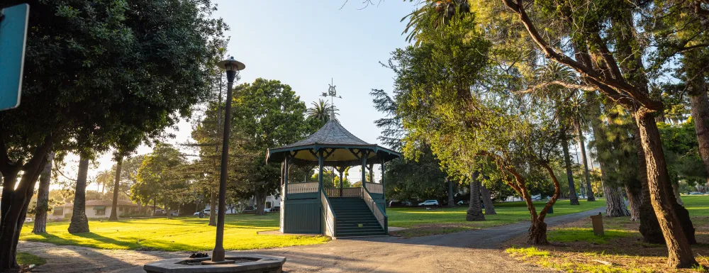 Alameda Bandstand with sun setting in the left of frame, pathways and trees illuminated.