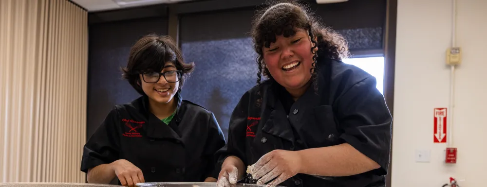 Two chef apprentices work together to bread chicken.