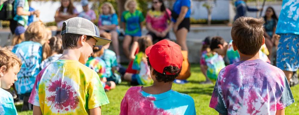 Campers in tie-dye shirts sit and focus on the camp counselors