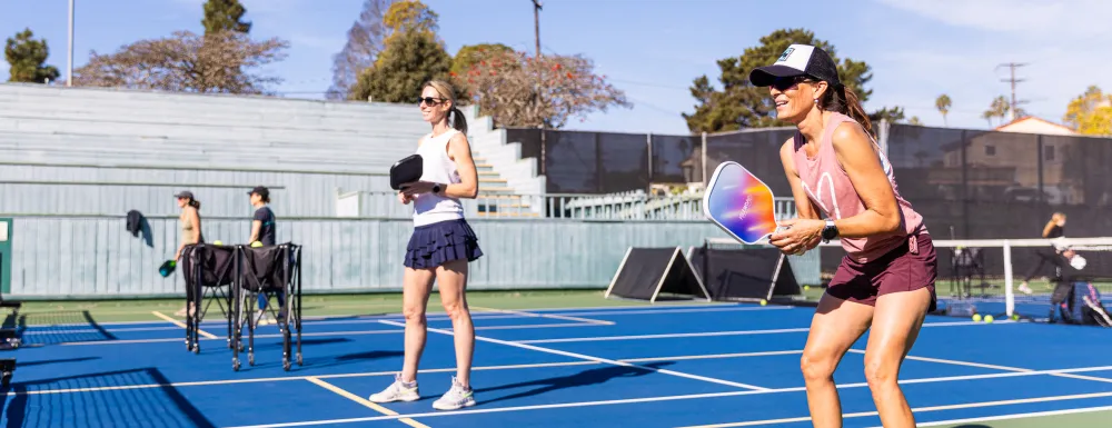 Two adult pickleball players smile as they await a serve