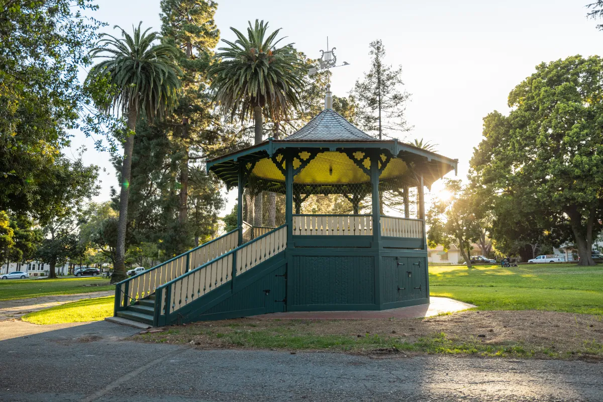 Alameda Bandstand with sun setting behind it, green grass and trees in background