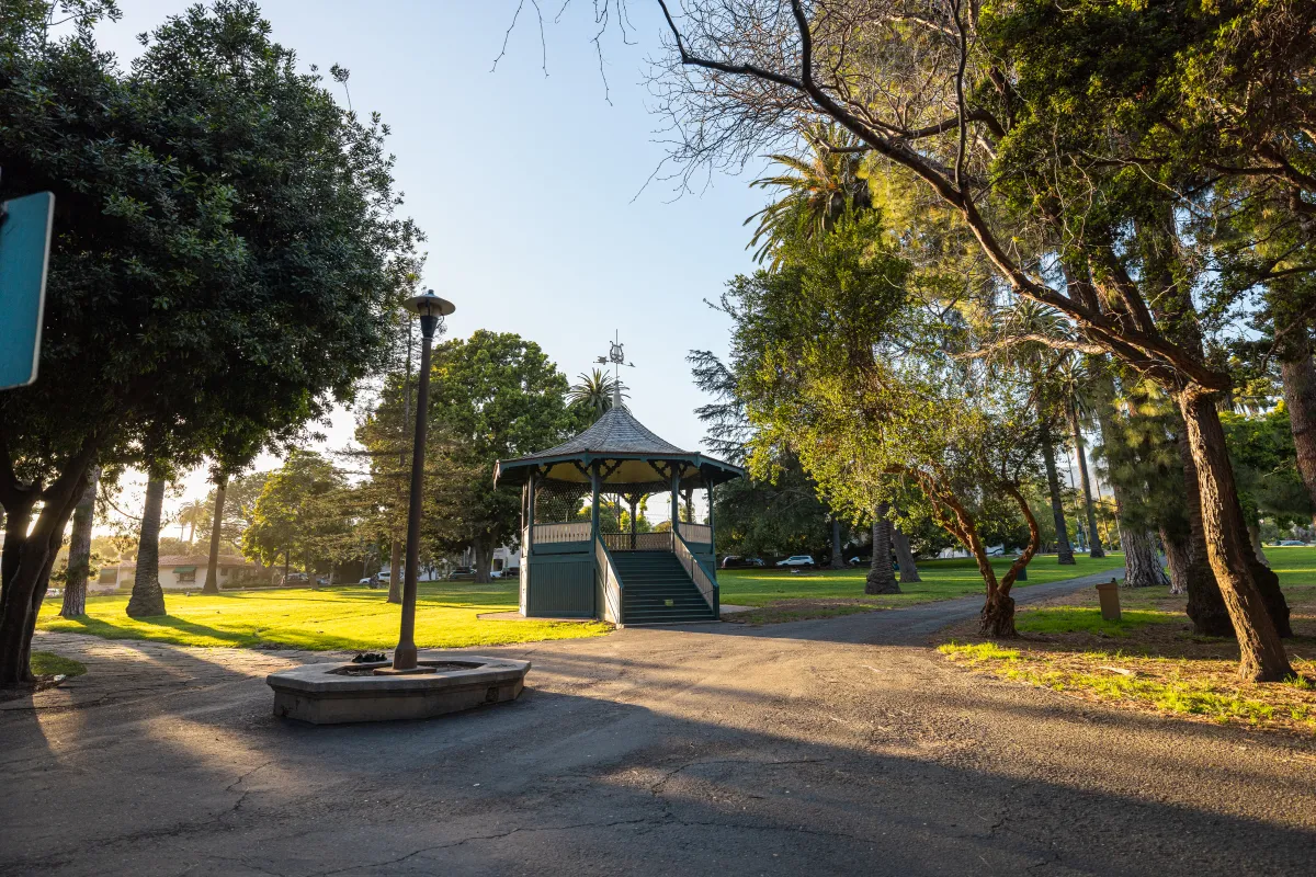 Alameda Bandstand with sun setting in the left of frame, pathways and trees illuminated.