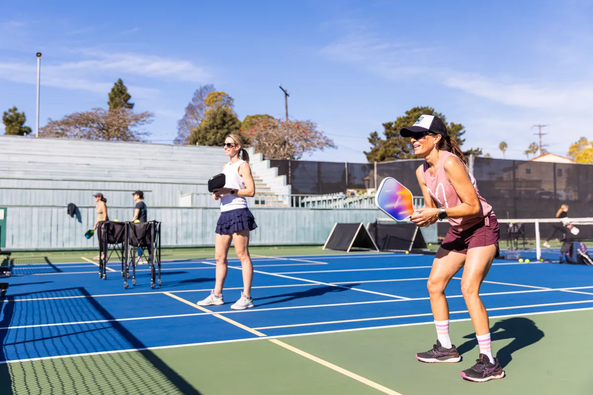 Two adult pickleball players smile as they await a serve