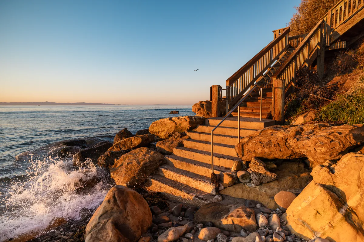 The bottom of Shoreline Steps at golden hour with waves splashing onshore