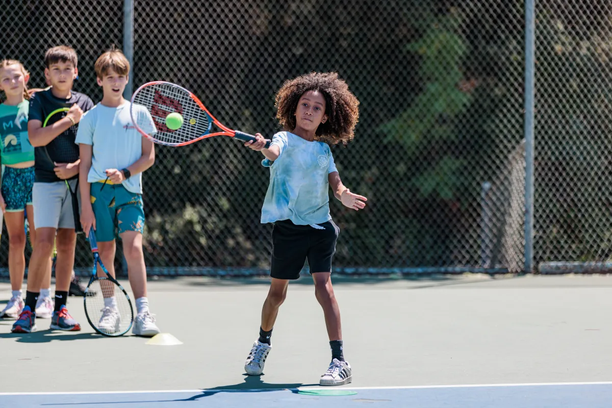 Tennis camper returns a serve during a drill