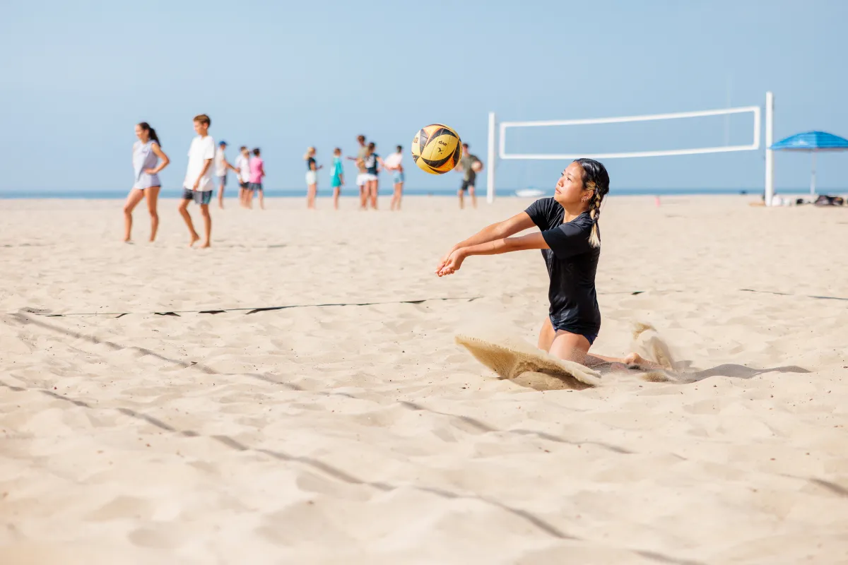 Beach volleyball camper dives in the sand to bump a volleyball