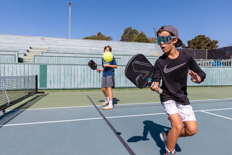 Camper backhands the ball over the net in pickleball camp 