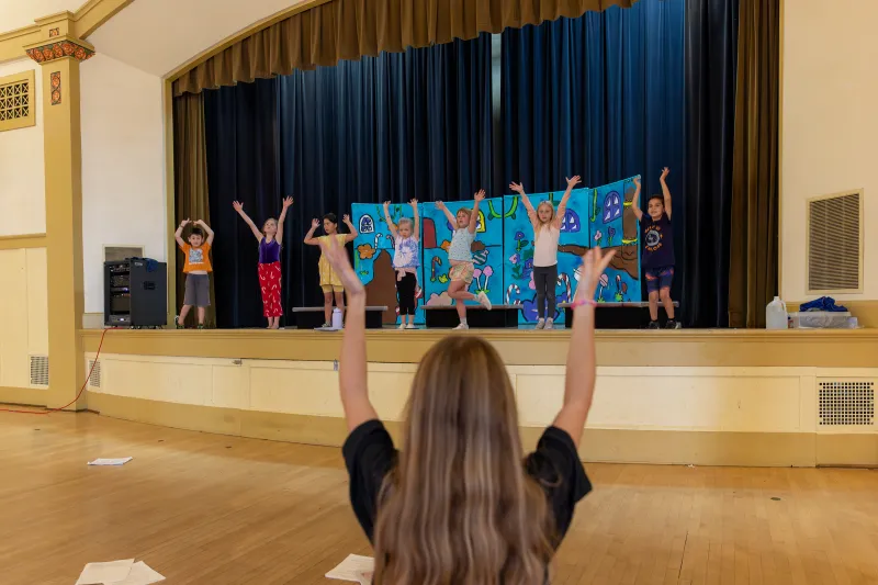 Campers perform on the stage with their counselor giving cues